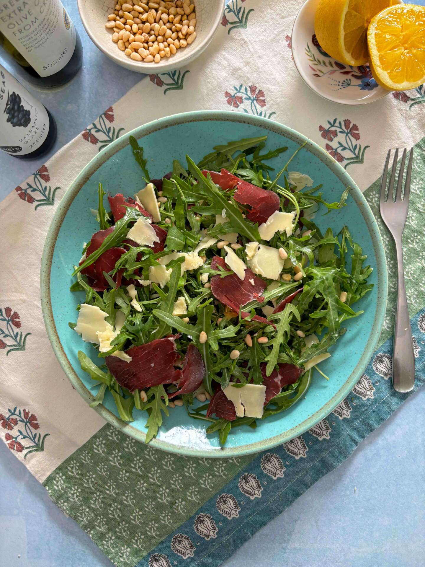 Bowl of rocket salad with bresaola and shaved cheddar on a blue plate