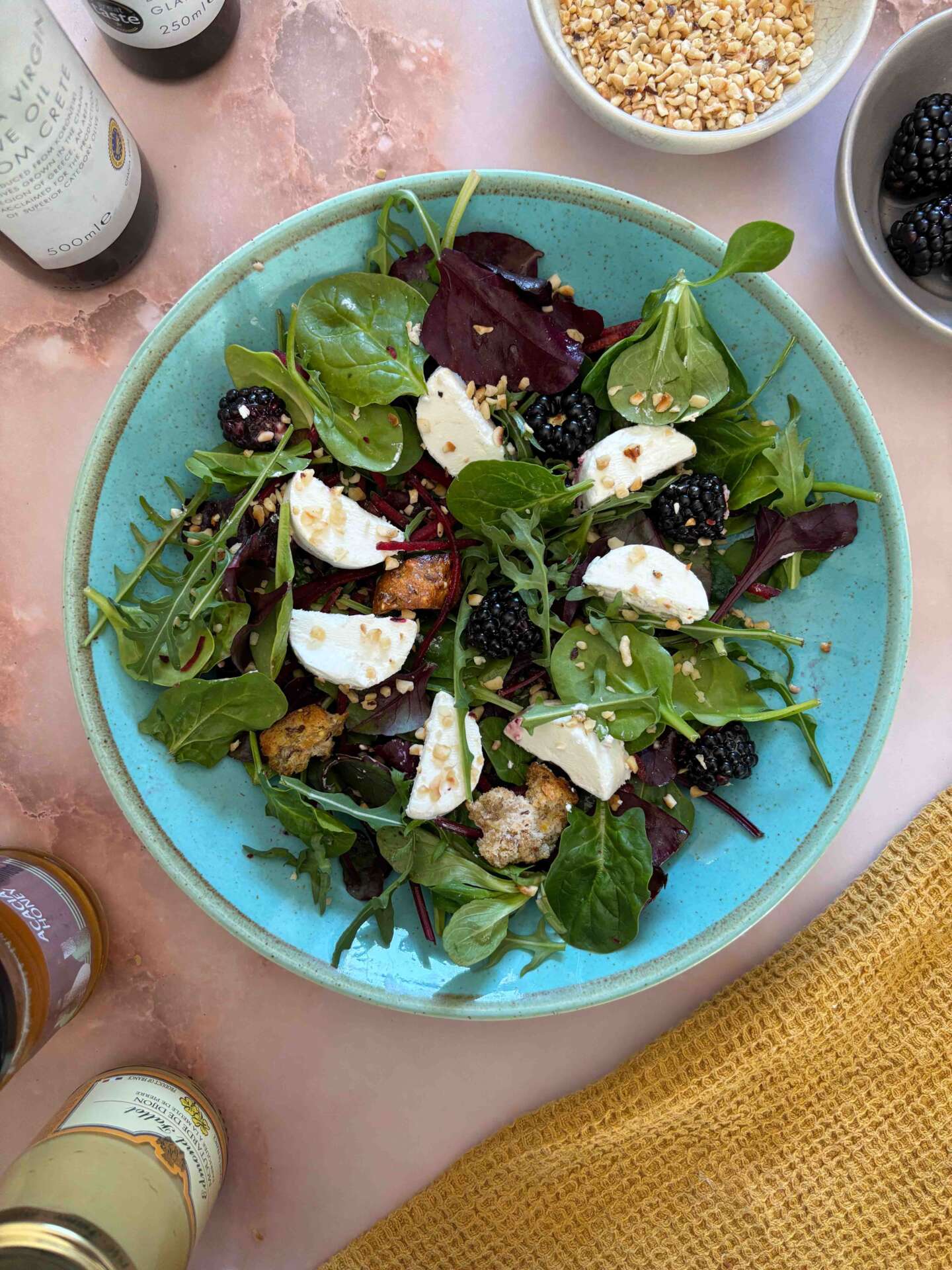 Bowl of leaf salad with goats cheese rounds and blackberries