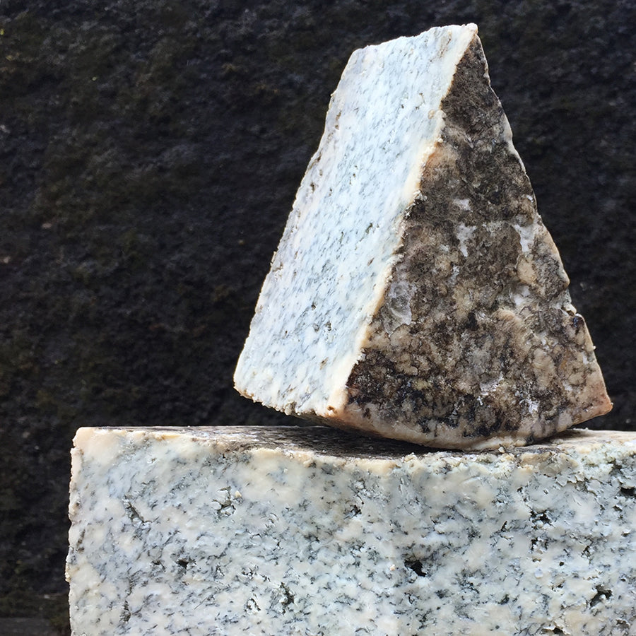 Two wedges of Cabrales blue cheese stacked on a dark stone