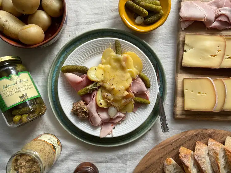 Plate of raclette poured over potatoes and ham with cornichons and bread