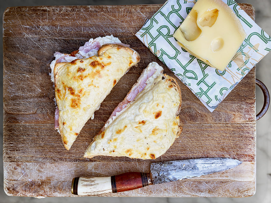 Croque monsieur cut in half on a wooden board with a knife