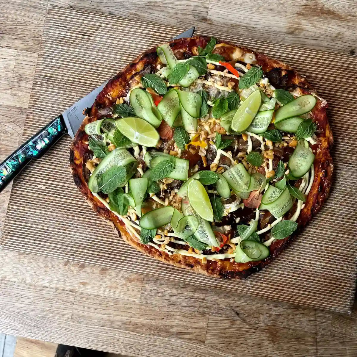 Duck pizza topped with spring onion and cucumber on a wooden board
