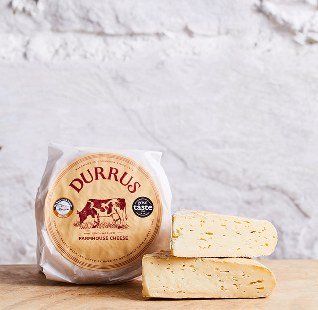 Wrapped Durrus cheese with slices cut from it against a white wall