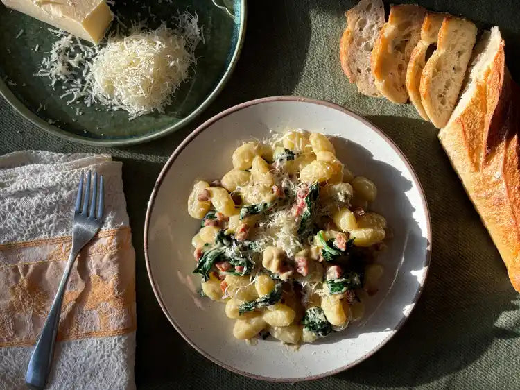 Bowl of gnocchi with pancetta and gorgonzola beside bread