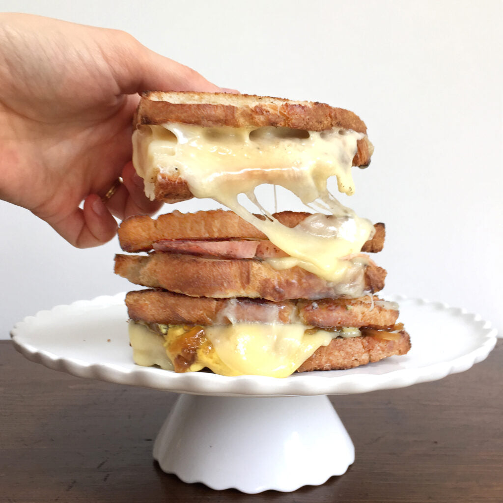 Hand lifting a stack of raclette grilled cheese sandwiches on a cake stand