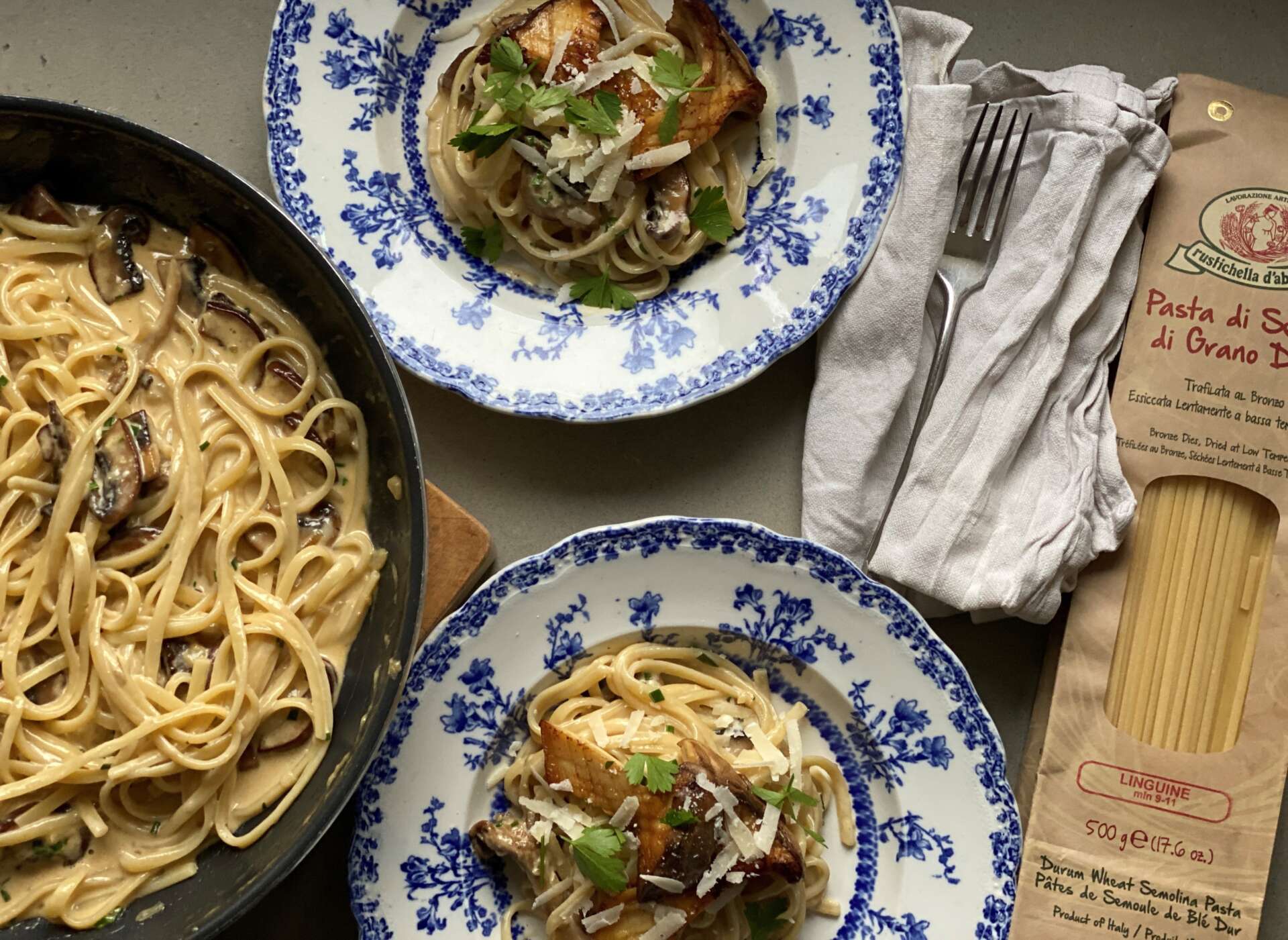 Pan and plates of linguine with autumn mushrooms beside dried pasta