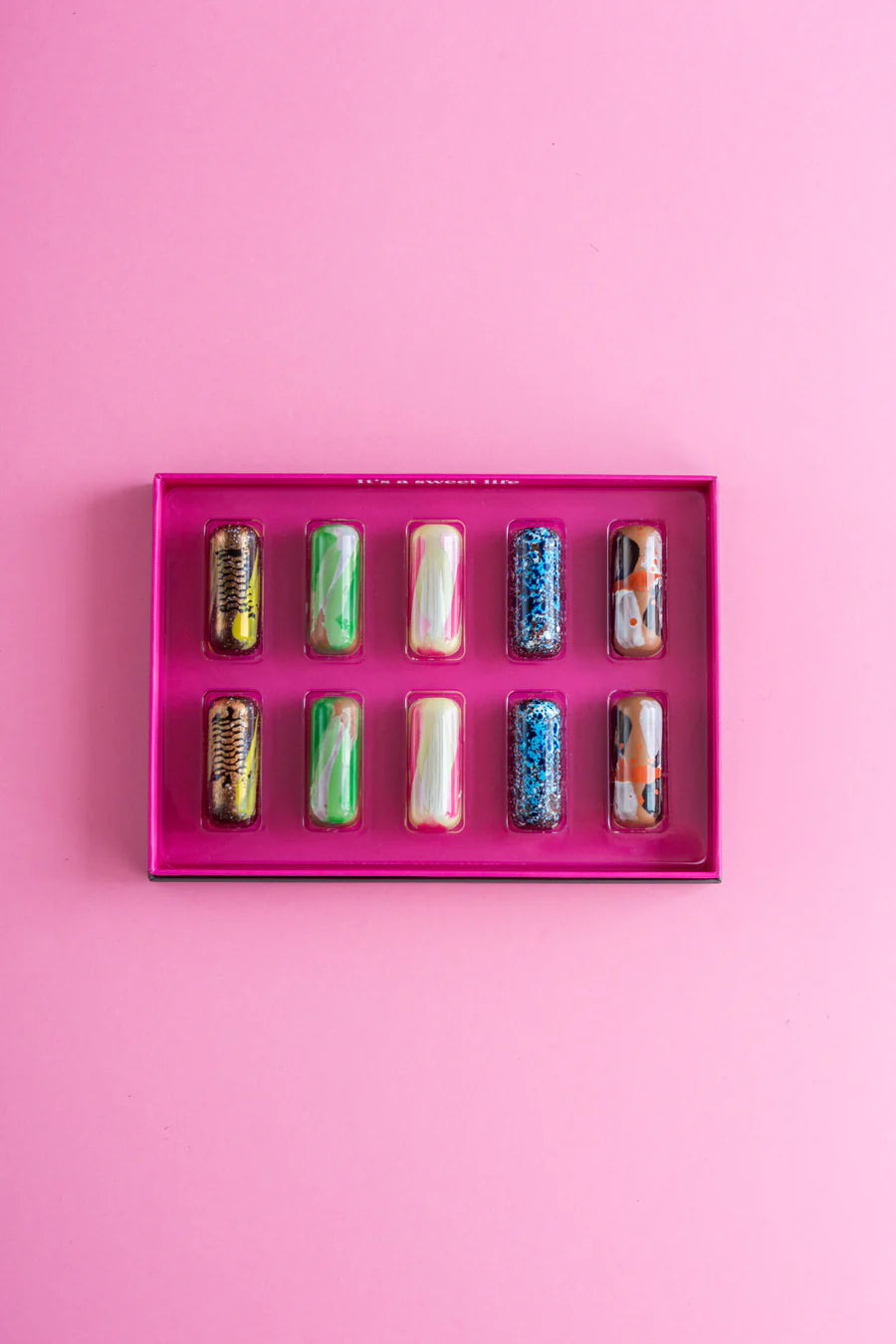 Assorted colorful nail polish bottles in a pink display case on a pink background