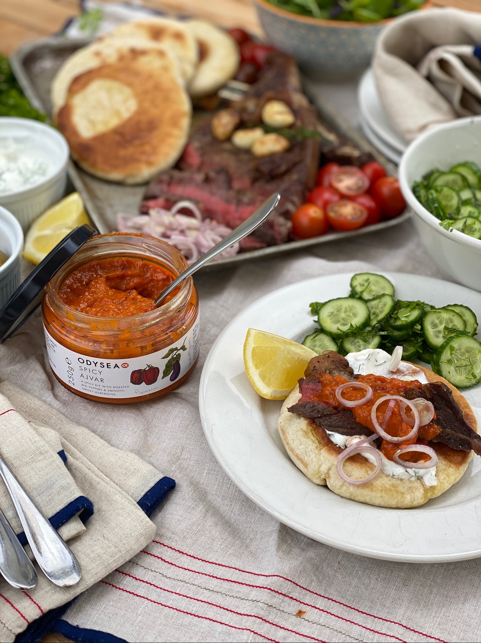 Plated dish with pita bread, meats, and vegetables on a table with a jar of Odyssey spread.