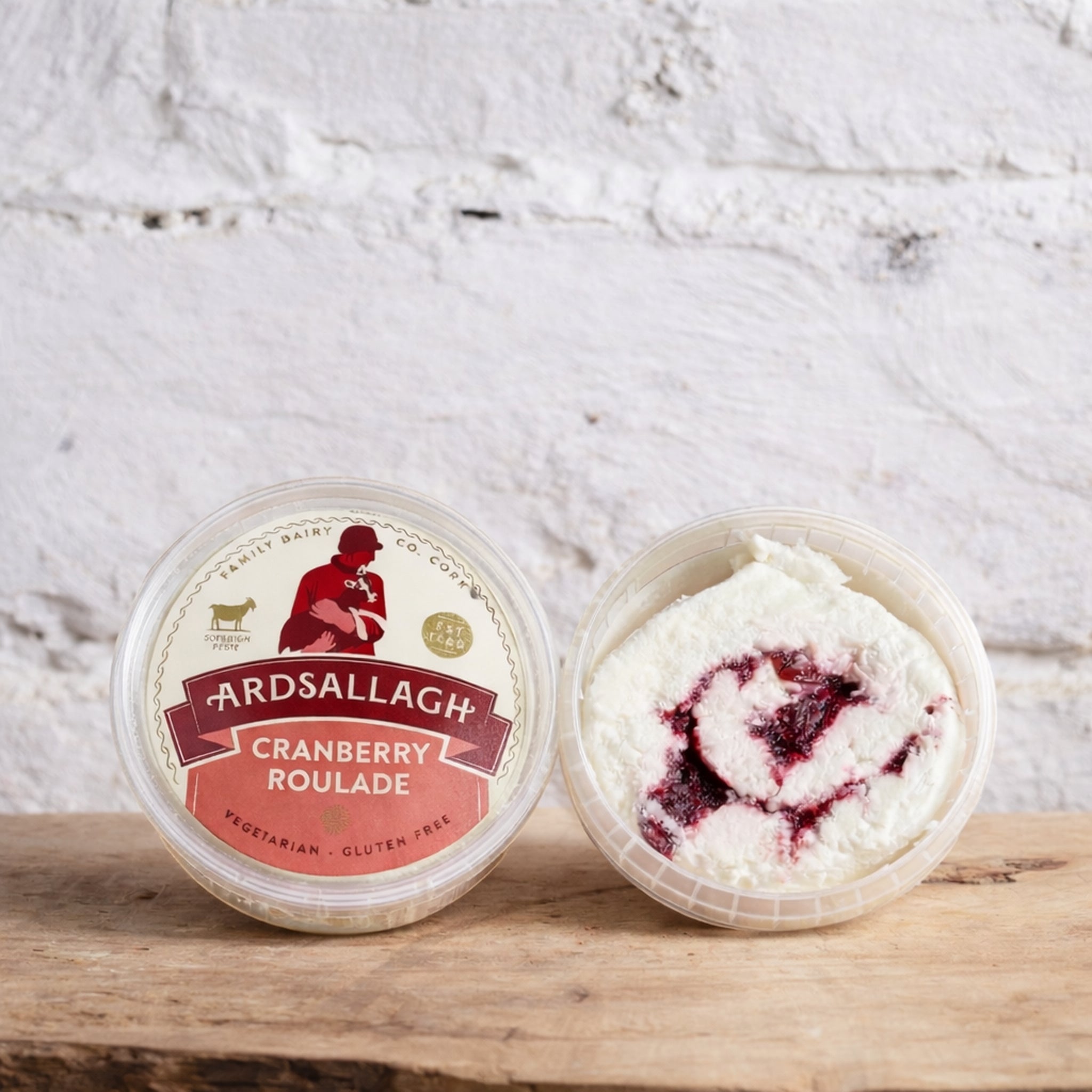 Two containers of Ardsallagh Cranberry Roulade on a wooden surface with a white textured background