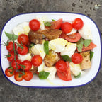 Salad with cherry tomatoes, bread, and herbs on a white plate with blue rim.