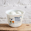 Container of Bufala mozzarella cheese on a wooden surface with a white textured background