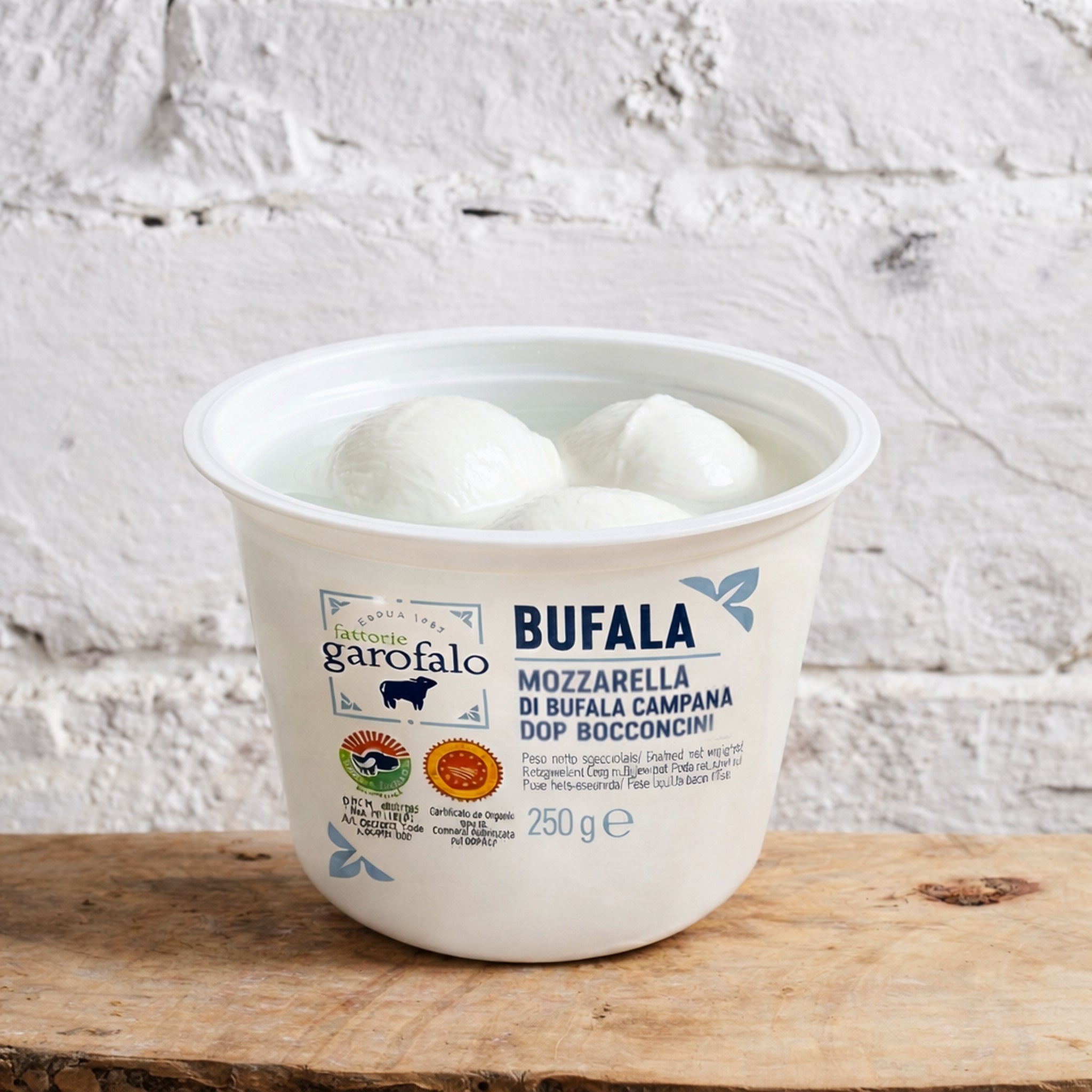 Container of Bufala mozzarella cheese on a wooden surface with a white textured background