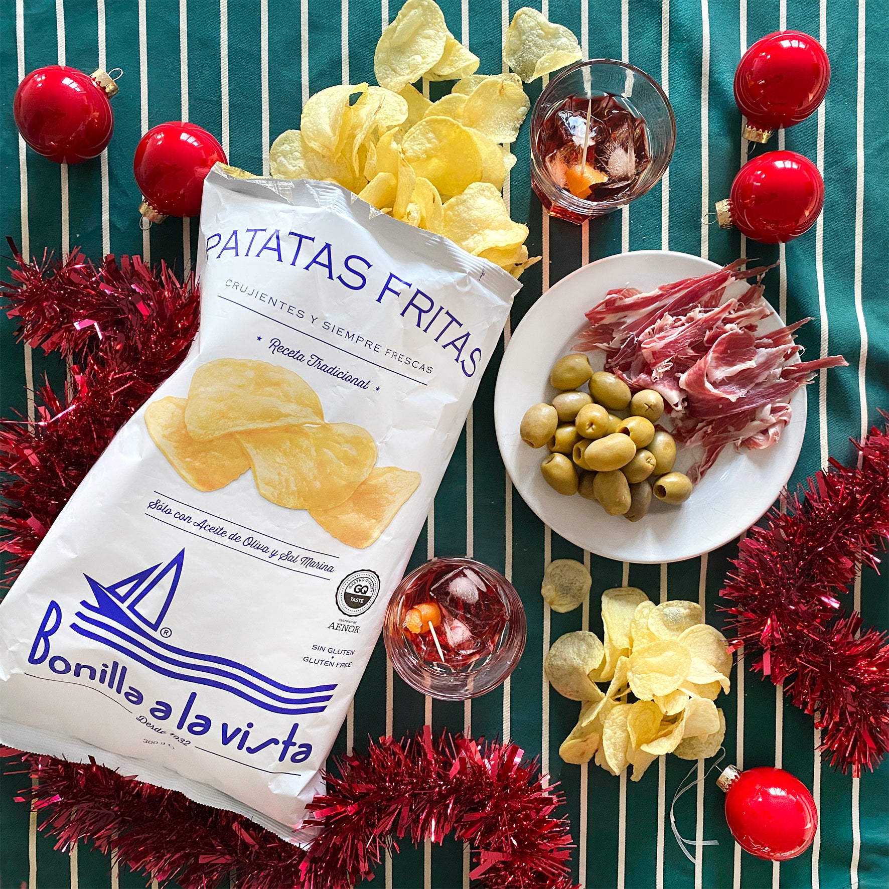 Packaged potato chips with a plate of cured meats, olives, and garnishes on a festive background.