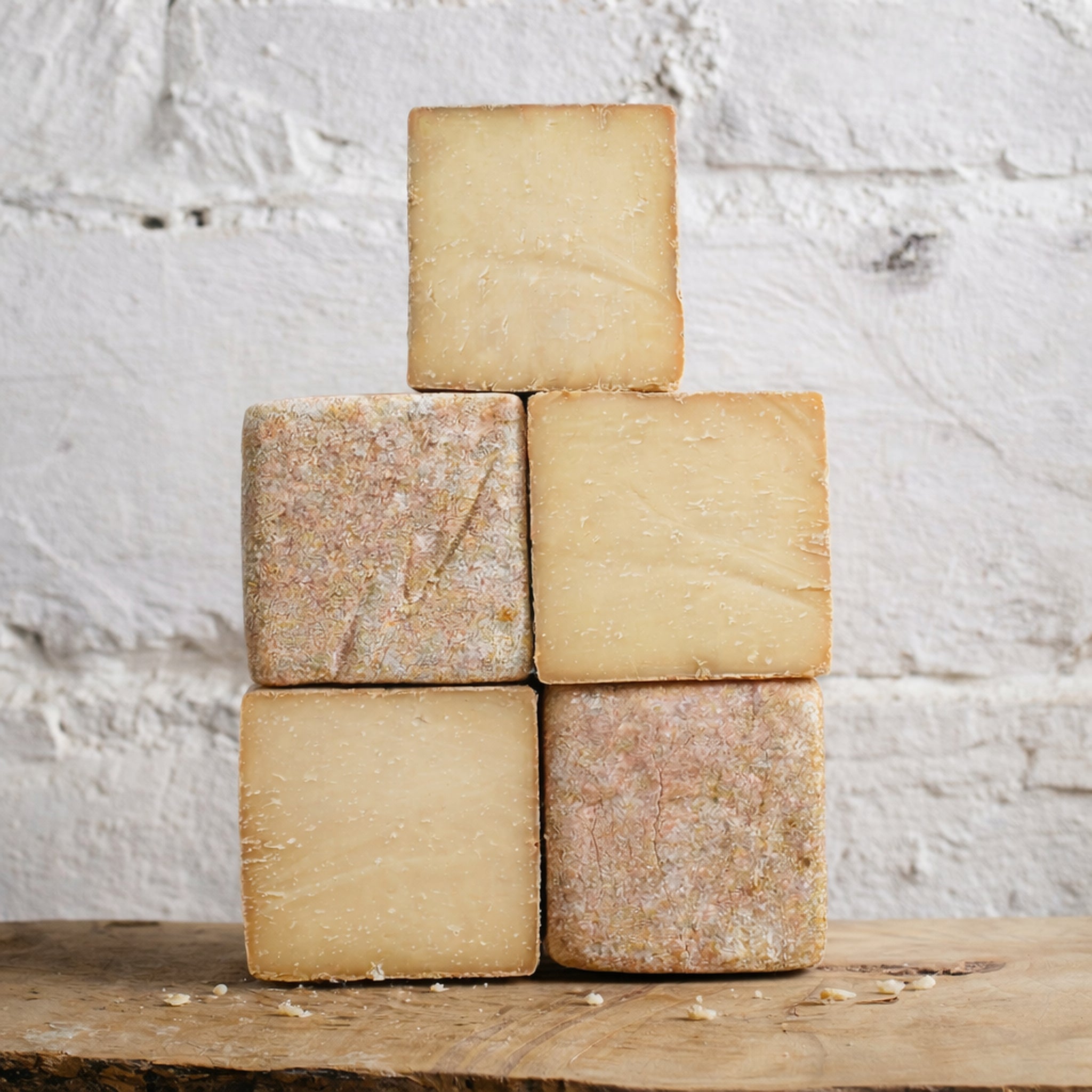 Five square pieces of cheese stacked on a wooden surface with a white textured background