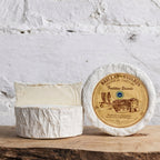 Two rounds of Brillat-Savarin cheese on a wooden surface with a textured white background