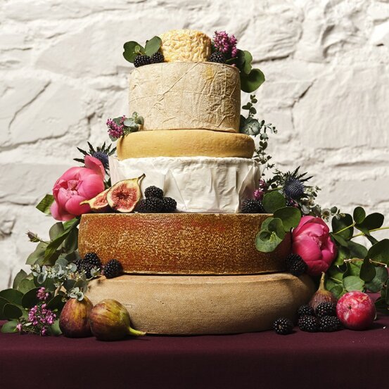 Large tiered cheese celebration cake decorated with pink roses, figs and berries