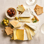 Assorted cheeses on a platter with crackers, olives, and a knife on a light background