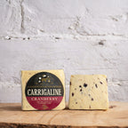 Carrigaline Cranberry cheese with packaging on a wooden surface against a white brick wall.
