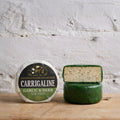 Round of Carrigaline garlic and herb cheese in green wax beside its labelled wheel