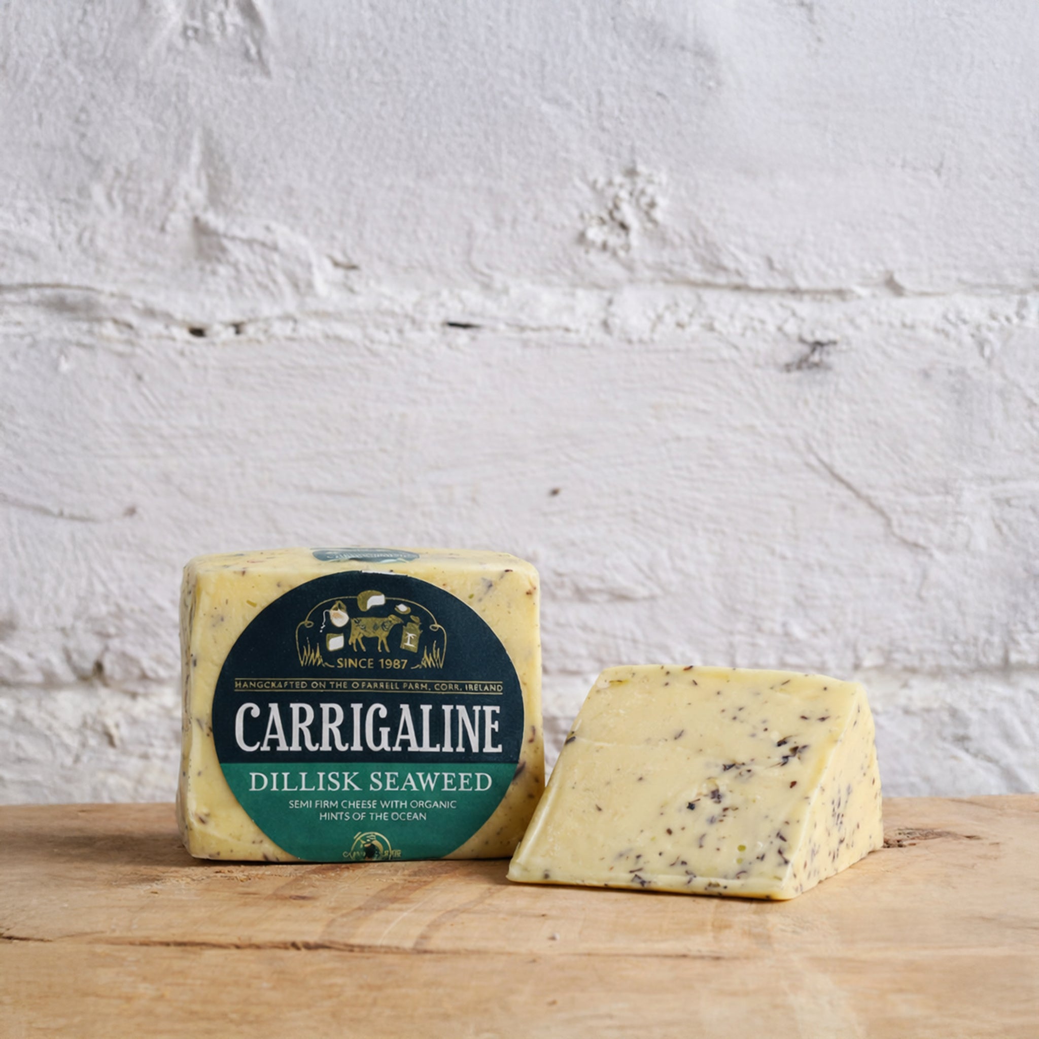 Carrigaline Dillisk Seaweed cheese with packaging on a wooden surface against a white brick wall.