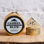 Cashel Blue cheese with a piece cut off, displayed on a wooden board.