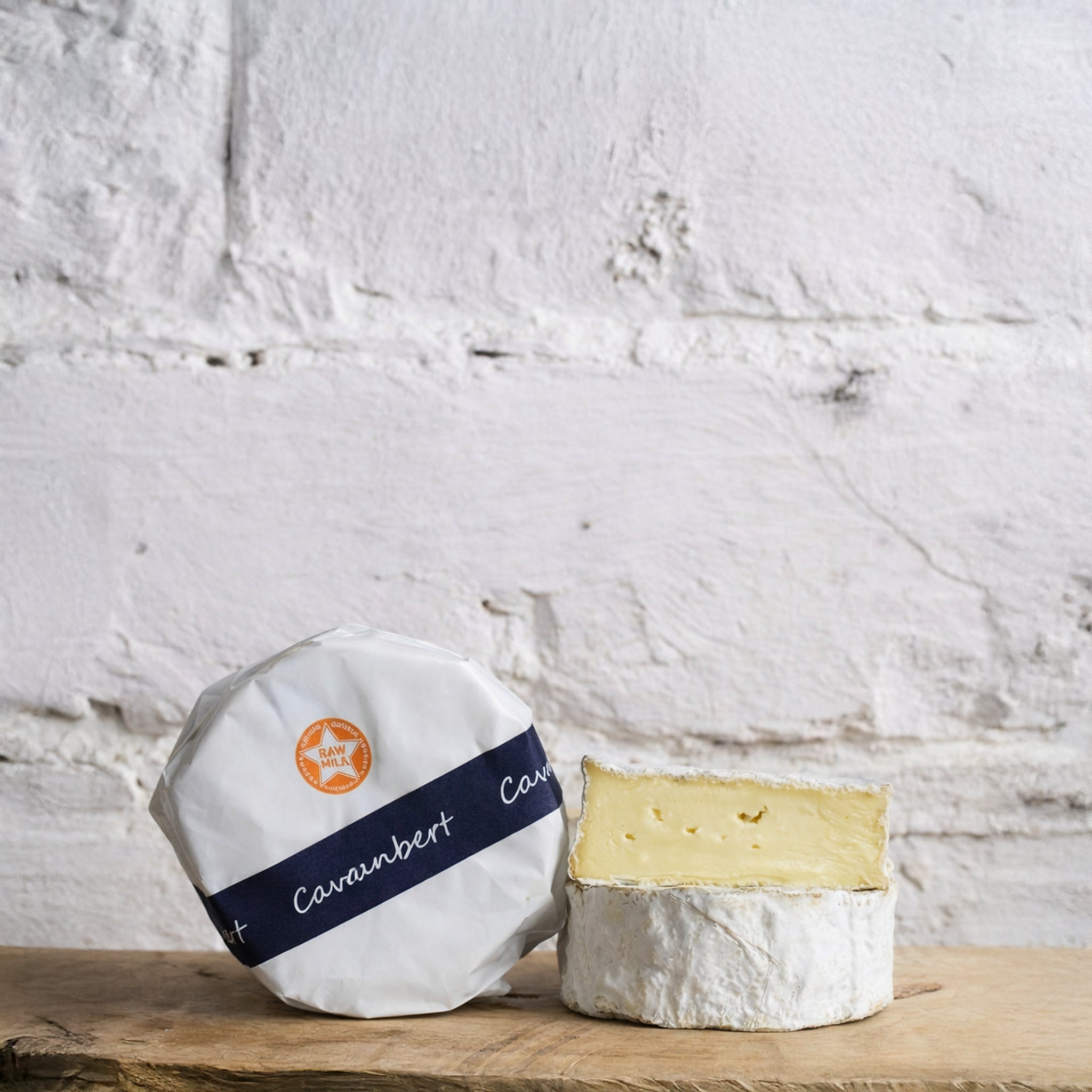 Two pieces of Camembert cheese on a wooden surface with a white textured wall background.
