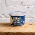 Container of Crème Fraçoise d'Isigny on a wooden surface with a light gray brick wall background