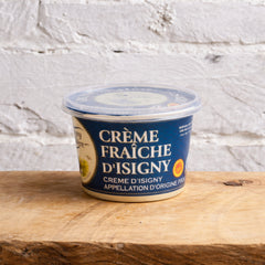 Container of Crème Fraçoise d'Isigny on a wooden surface with a light gray brick wall background