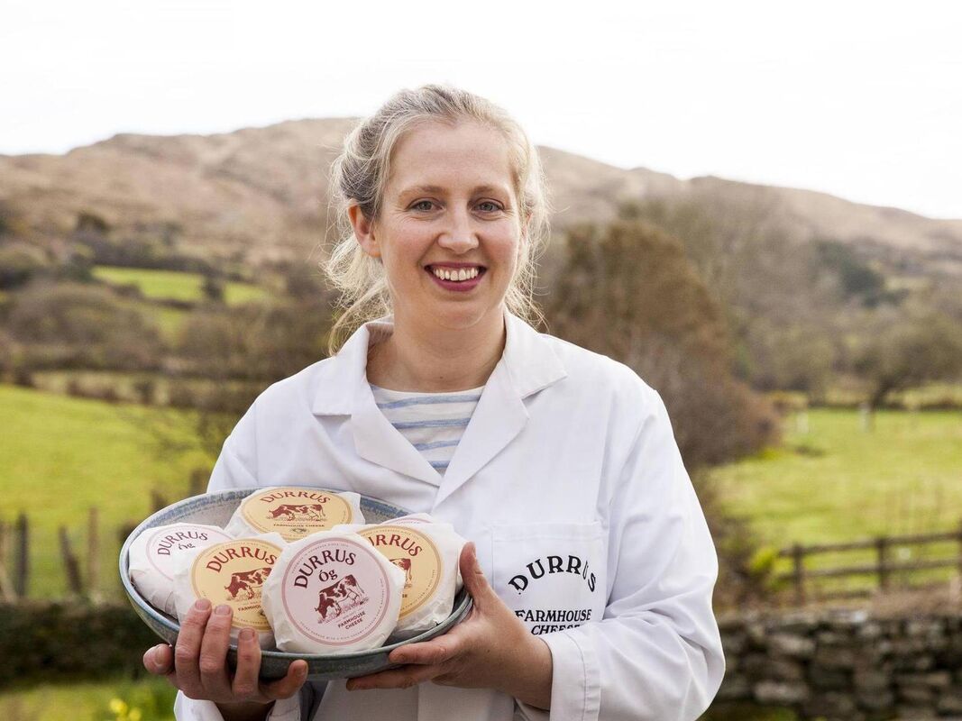 Woman holding a tray of Durrus cheese in a scenic outdoor setting