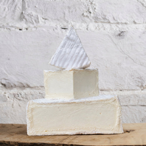 Three blocks of cheese stacked on a wooden surface with a marble background