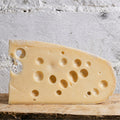 Swiss cheese wedge on a wooden board with a white stone background