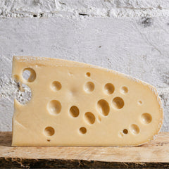 Swiss cheese wedge on a wooden board with a white stone background