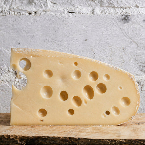 Swiss cheese wedge on a wooden board with a white stone background