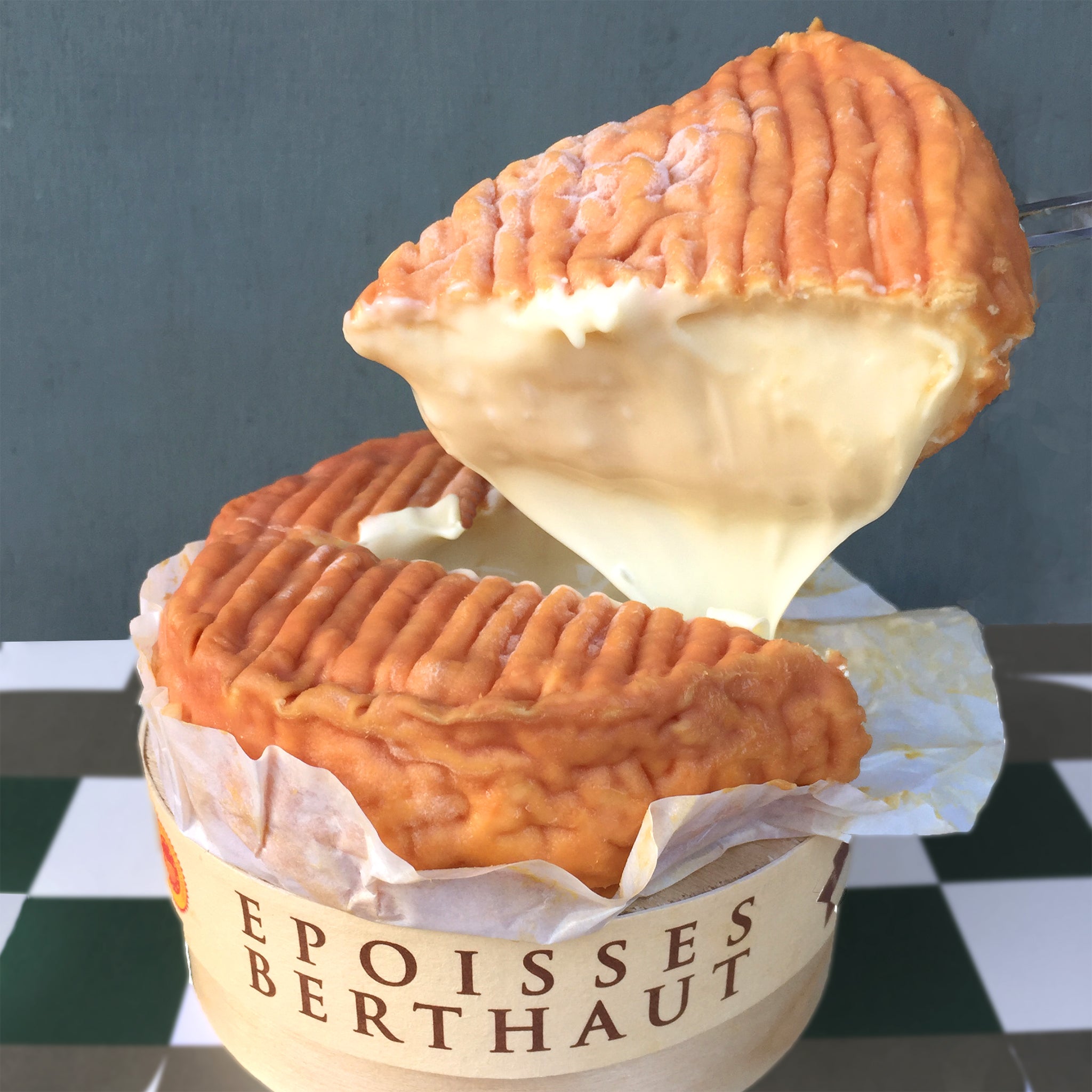 Two Epoisses Berthaut cheese wheels stacked on top of each other with a checkered background.