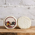 Round cheese with a label on a wooden surface against a textured white wall