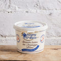Isigny de Mère cheese container on a wooden surface with a white brick wall background