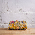 Loaf of bread with colorful toppings on a wooden surface against a white brick wall.