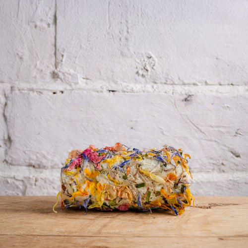 Loaf of bread with colorful toppings on a wooden surface against a white brick wall.