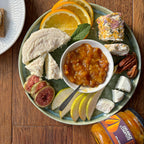 Platter of assorted cheeses, fruits, and a bowl of jam on a wooden table.