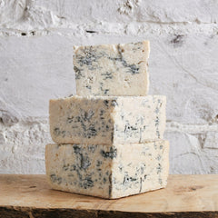 Three blocks of blue cheese stacked on a wooden surface with a white stone background