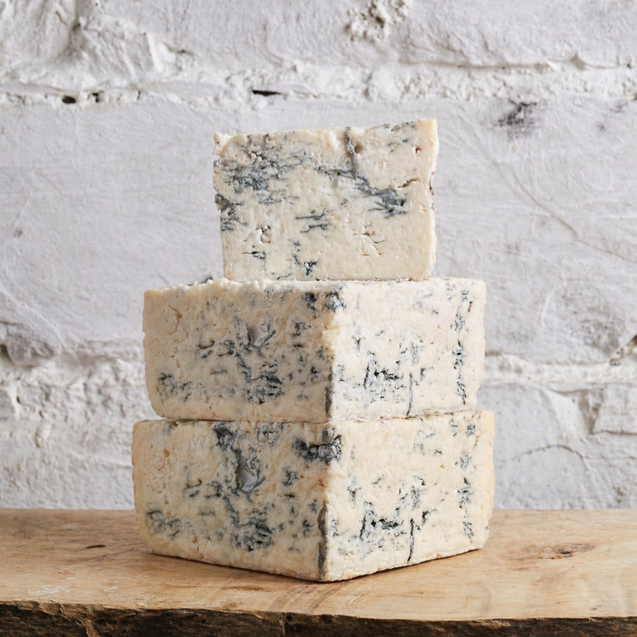Three blocks of blue cheese stacked on a wooden surface with a white stone background