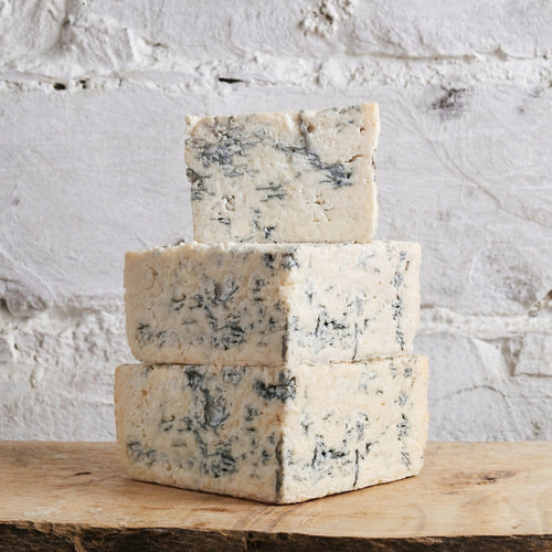 Three blocks of blue cheese stacked on a wooden surface with a white stone background