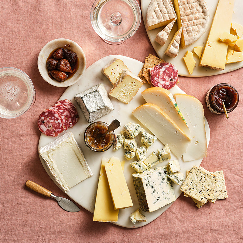 Assorted cheeses with accompaniments on a marble board on a pink tablecloth.