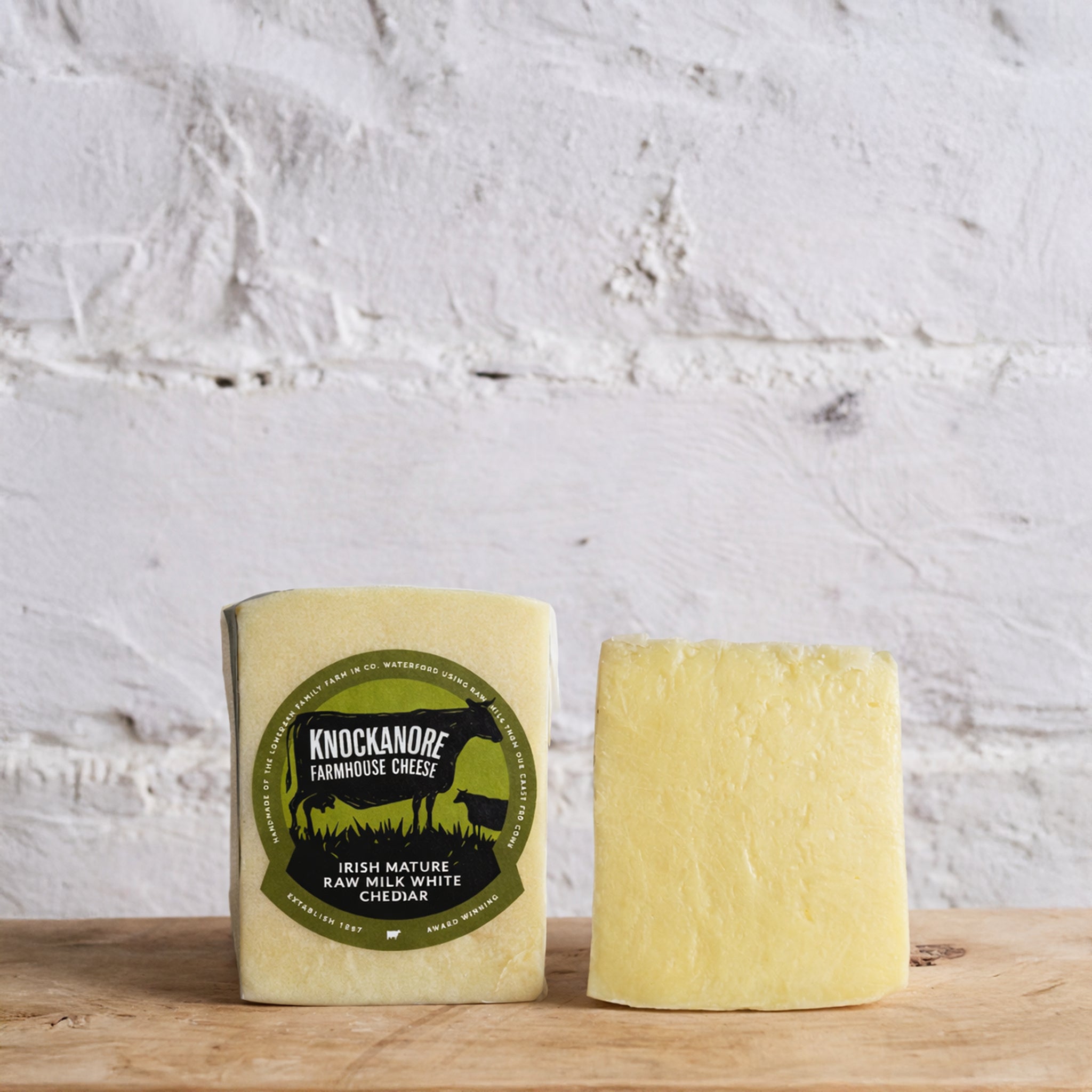 Two blocks of cheese with a Knockanore Farmhouse Cheese label on a wooden surface.