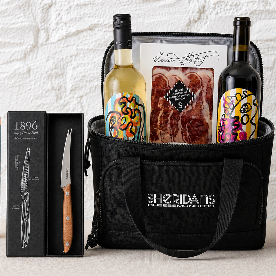 Black tote bag with Sheridan's Cheesemongers branding, containing two bottles of wine and a package of meat, next to a box and knife set.