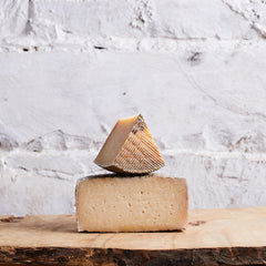 Two blocks of cheese stacked on a wooden surface with a white marble background