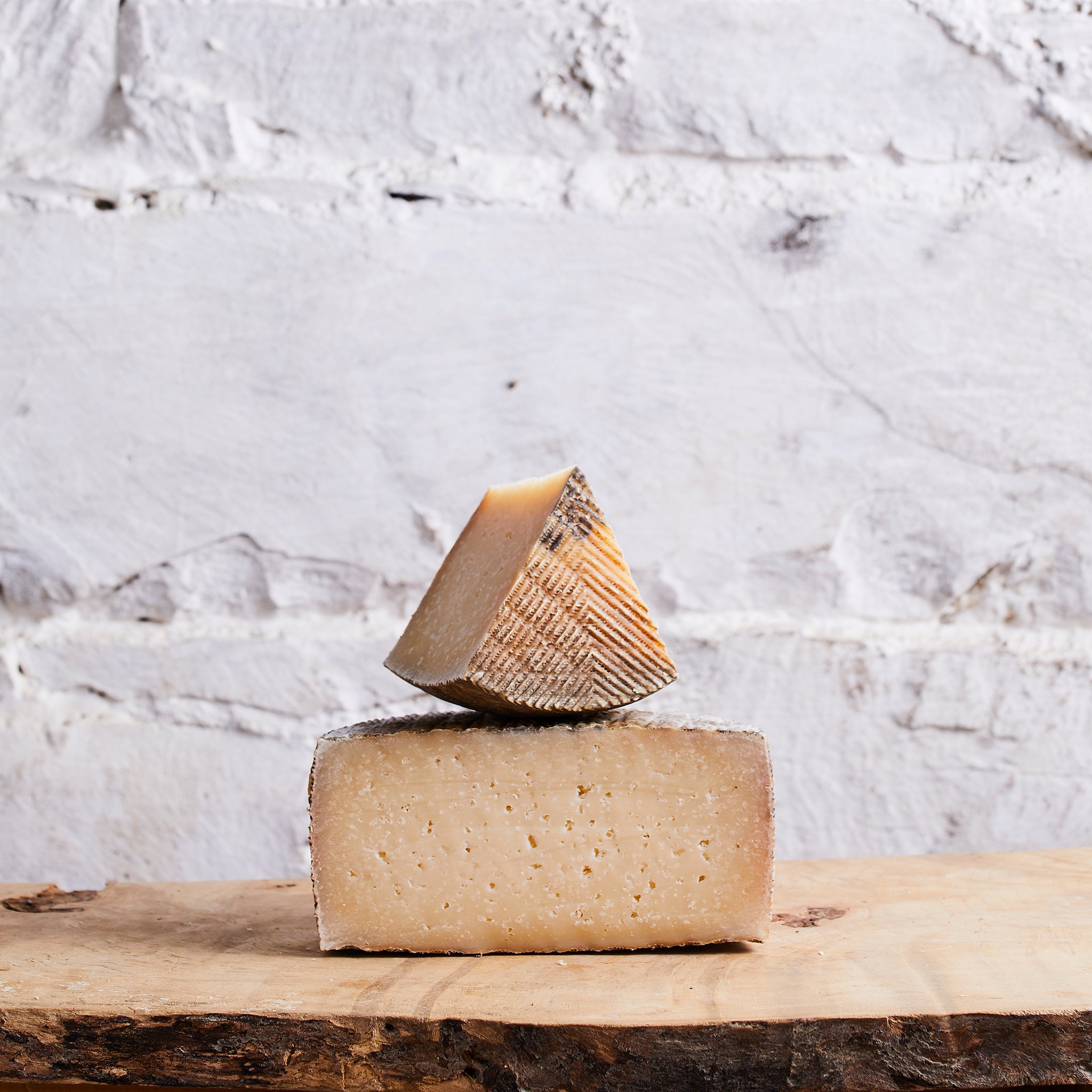 Two blocks of cheese stacked on a wooden surface with a white marble background
