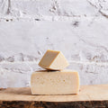 Two blocks of cheese stacked on a wooden board with a marble background