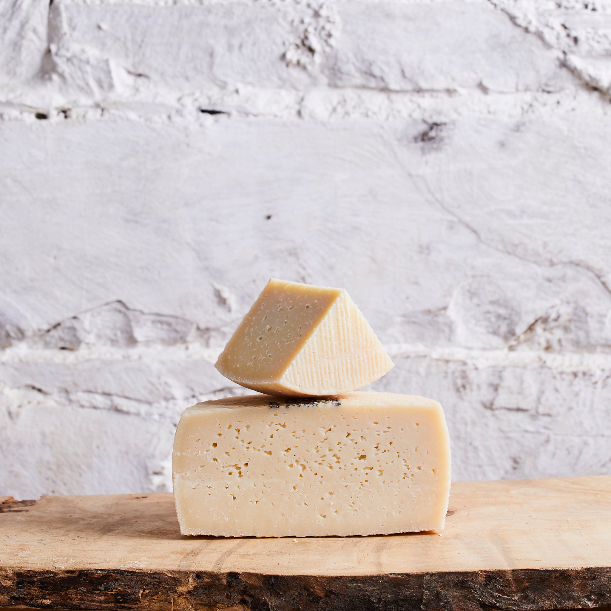 Two blocks of cheese stacked on a wooden board with a marble background