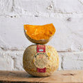 Mimolette cheese with a pumpkin half on top against a textured white wall.